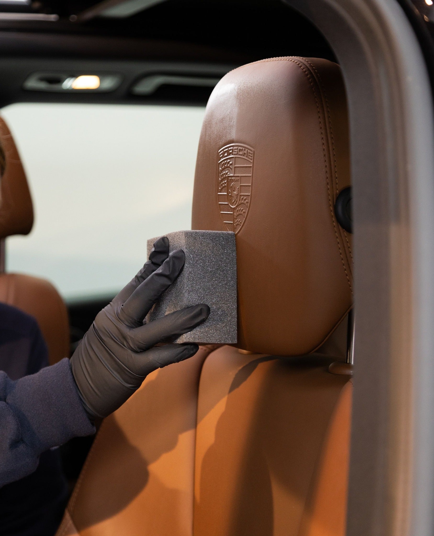A man wearing gloves performing car interior cleaning, with a sponge to apply car dressing for a car detail. The man is use car cleaning products and a car wash kit