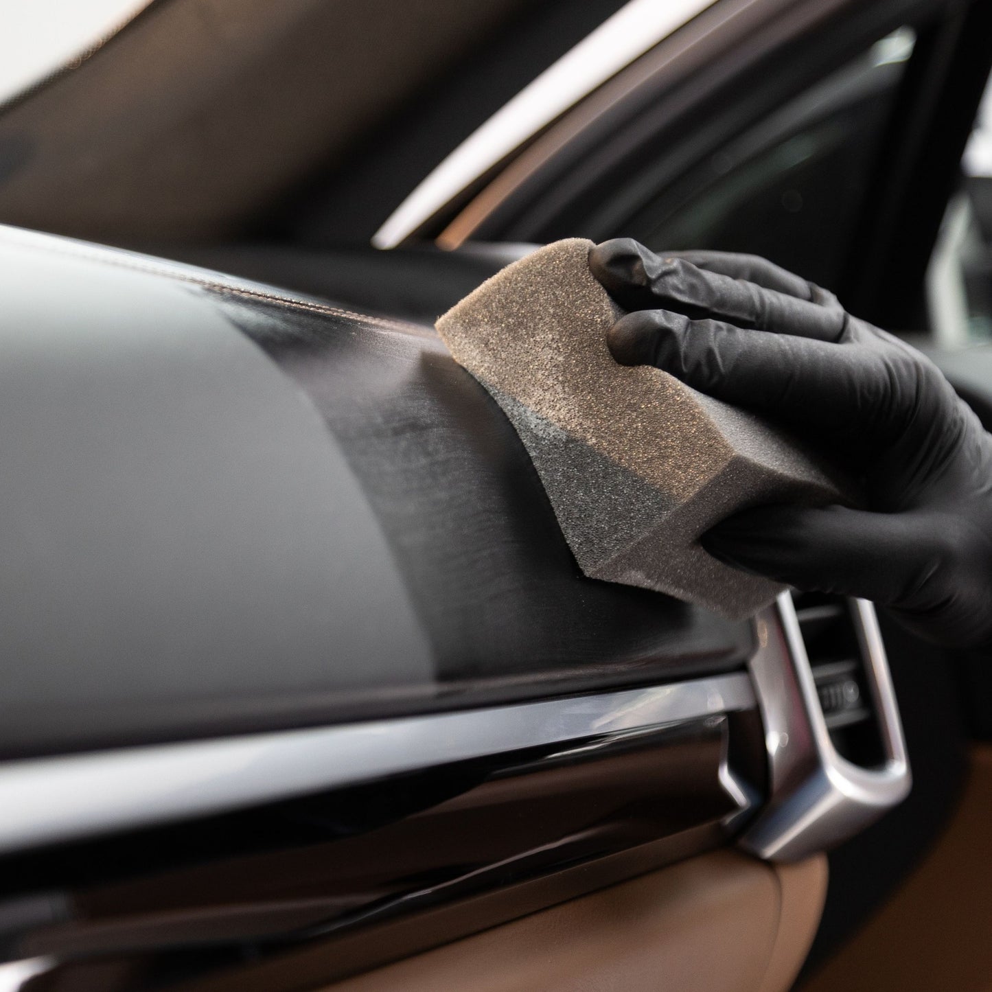 A man wearing gloves performing car interior cleaning. with a sponge to apply car dressing for a car detail. The man is car washing interior