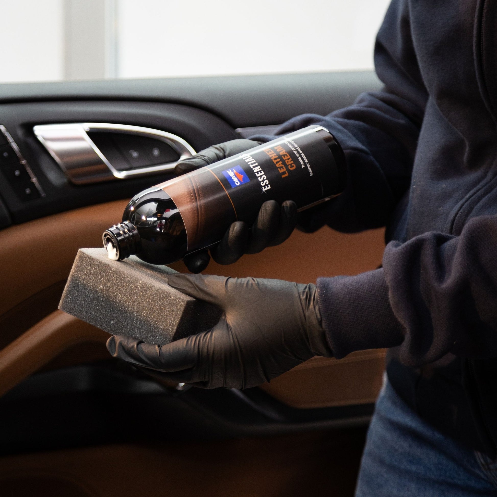 A man wearing gloves performing car interior cleaning, with a sponge to apply car dressing for a car detail. The man is use car cleaning products