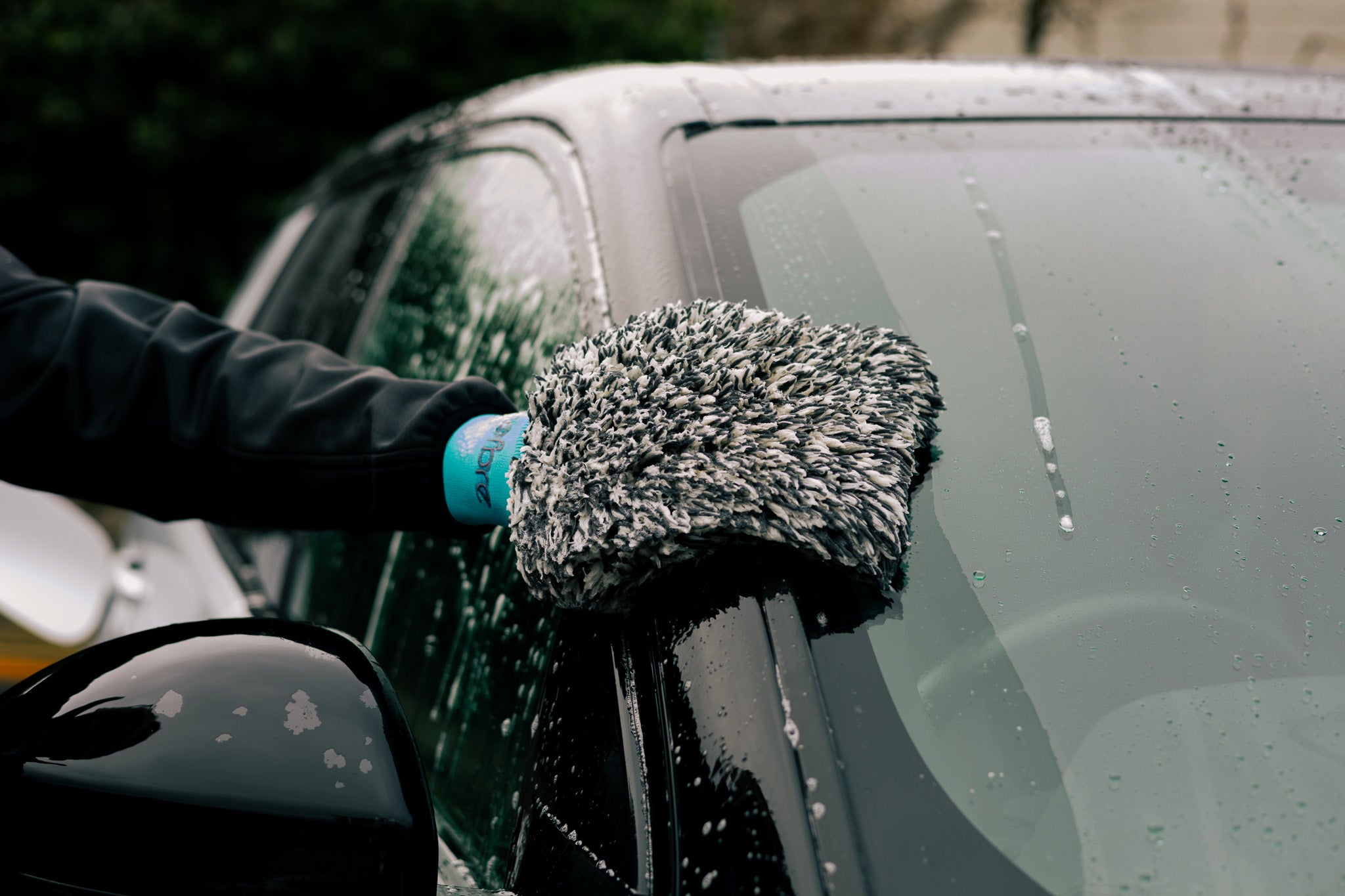 Person cleaning a car window with a microfibre wash mitt