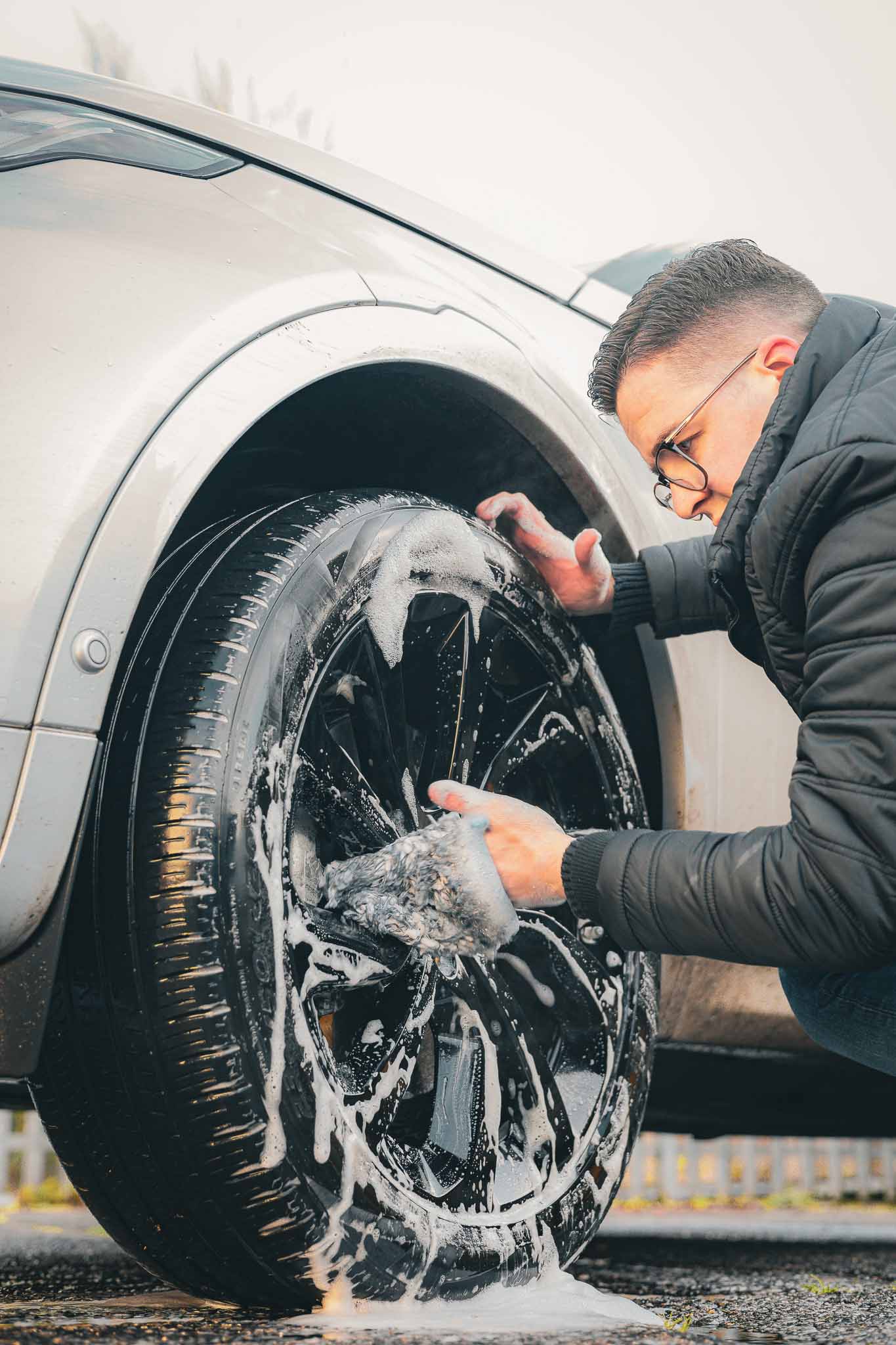 A discovery sport with pre wash snow foam on the wheel, a man cleaning the wheel in a car wash near me using car cleaning products exterior from imobi detail products in UK