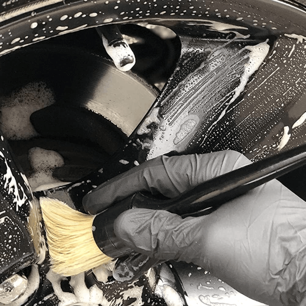 Person cleaning a car wheel with a car cleaning brushes
