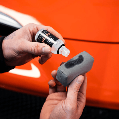 Car detailer applying ceramic coating to an applicator pad before protecting the paintwork of an orange car.