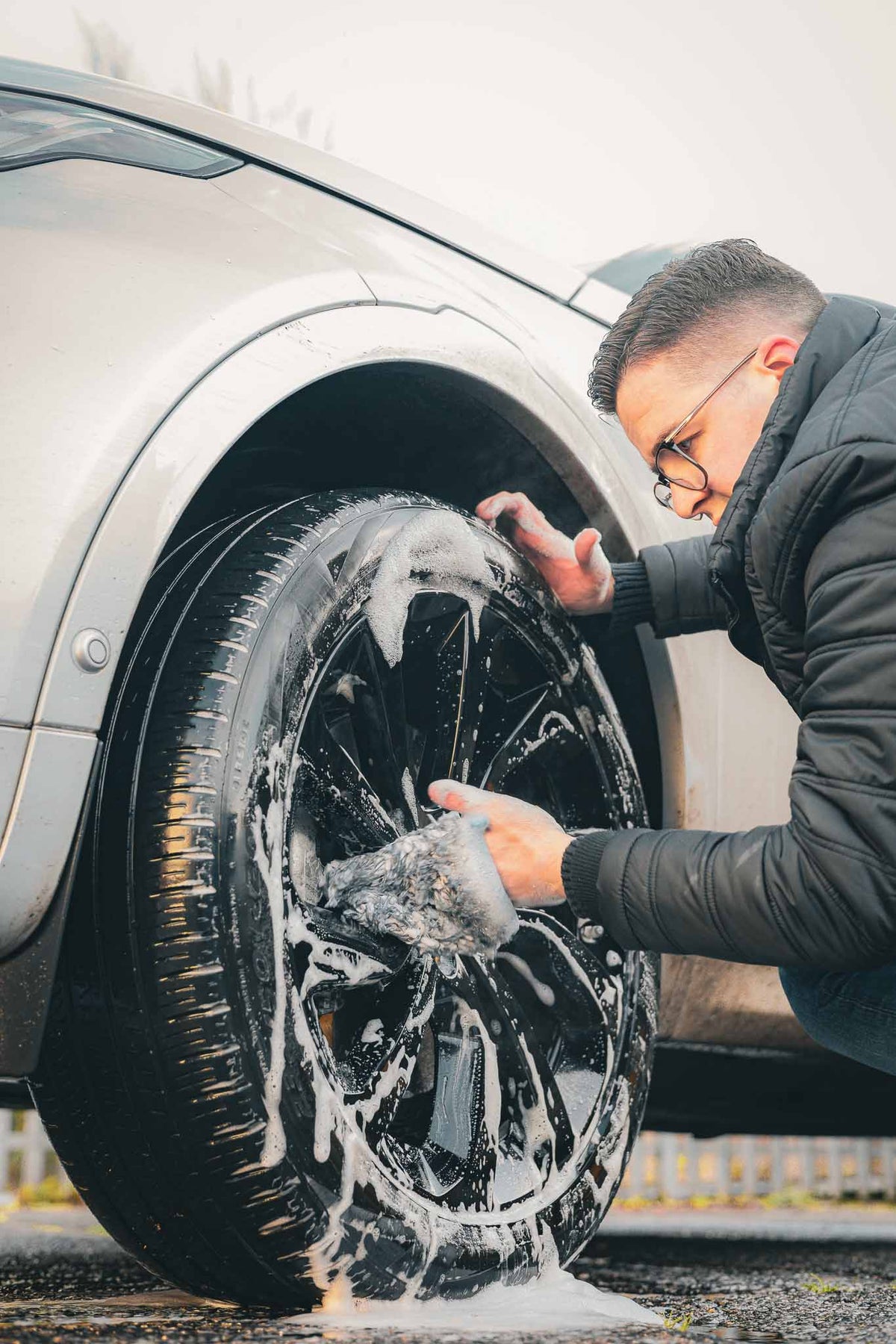 Professional detailer cleaning an alloy wheel with a microfibre wash mitt during a car wash. Safe wheel cleaning using pH-neutral car shampoo to remove brake dust, road grime and dirt as part of a professional car detailing and valeting process.