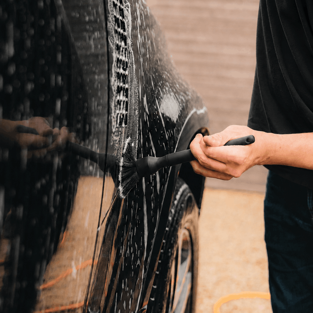 Person cleaning a black car with a car detailing brush