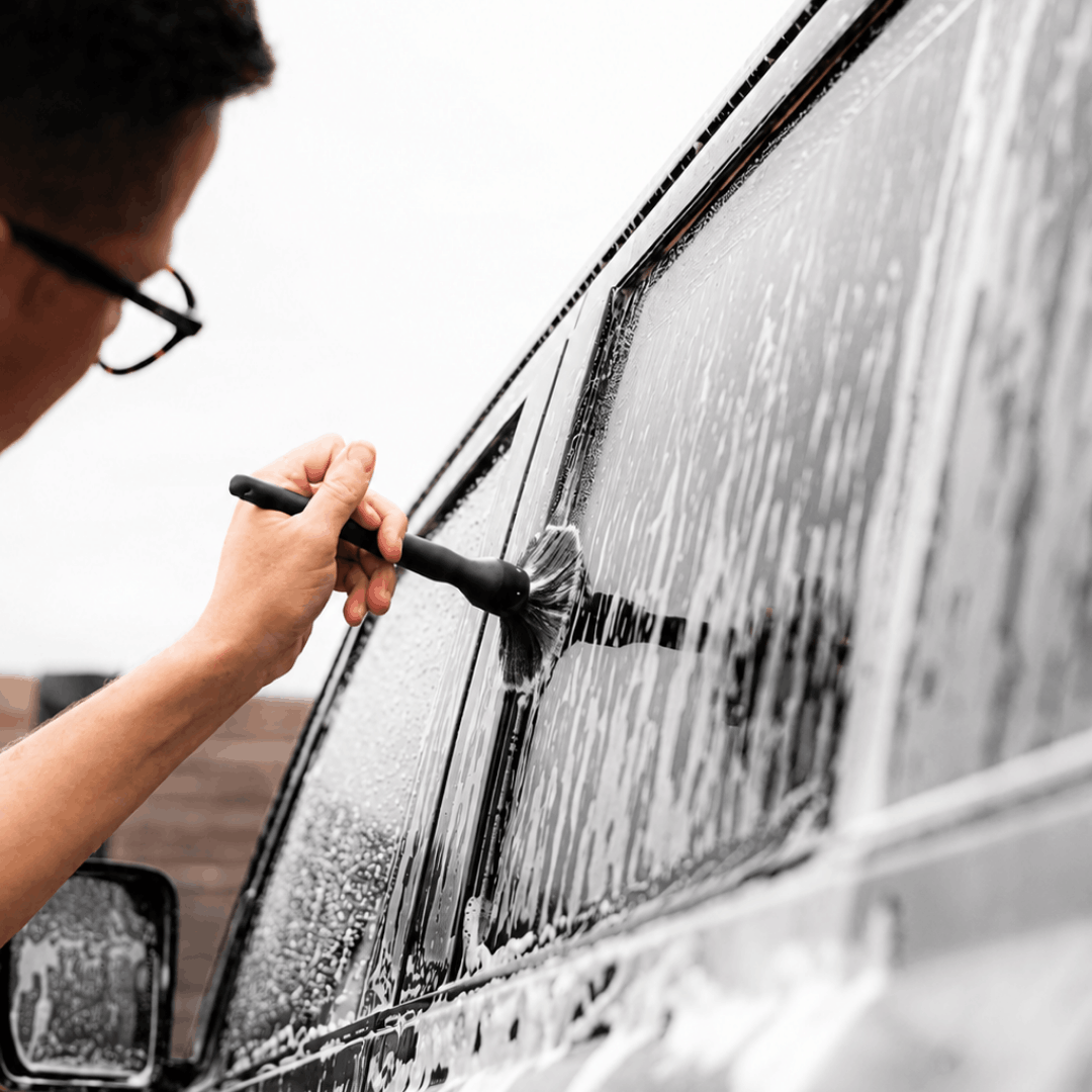 Person cleaning a car window with a car cleaning brush