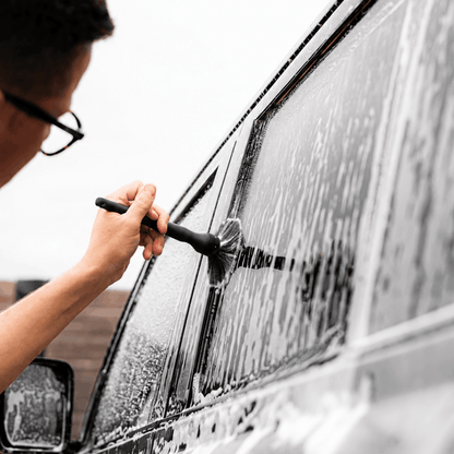 Person cleaning a car window with a car cleaning brush