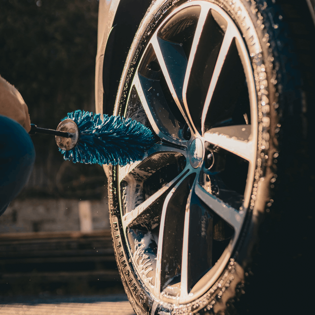 Blue wheel barrel brush cleaning a car alloy wheel during professional car detailing and wheel washing with car shampoo.