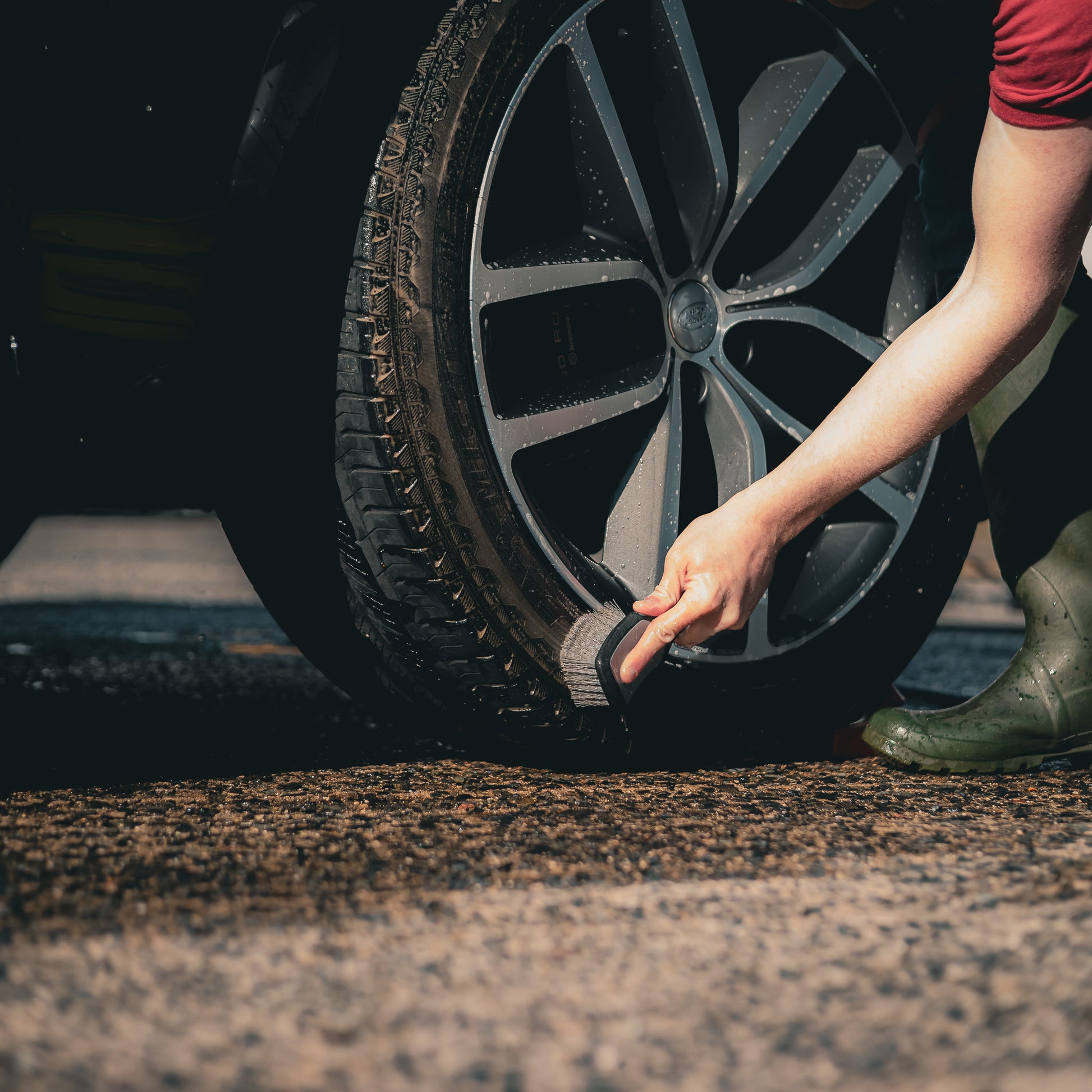 Person cleaning a car tyre with an Imobi tyre brush on a wet road