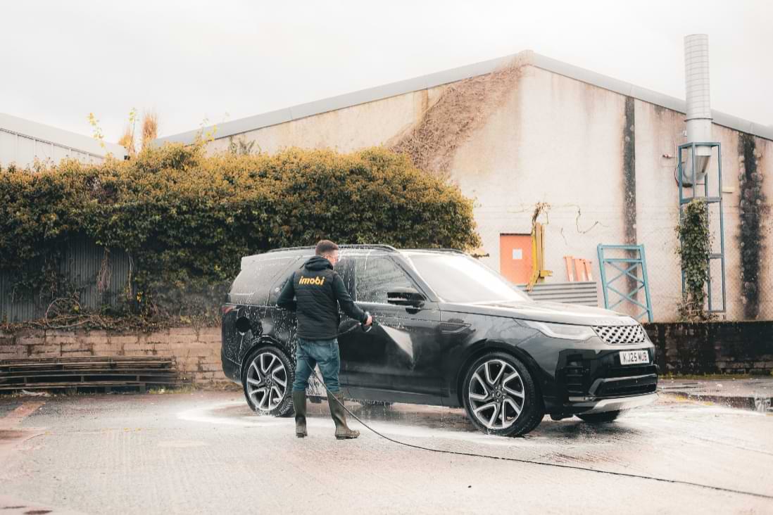 Imobi car detailer pressure rinsing snow foam from a black Land Rover Discovery during a professional exterior clean.