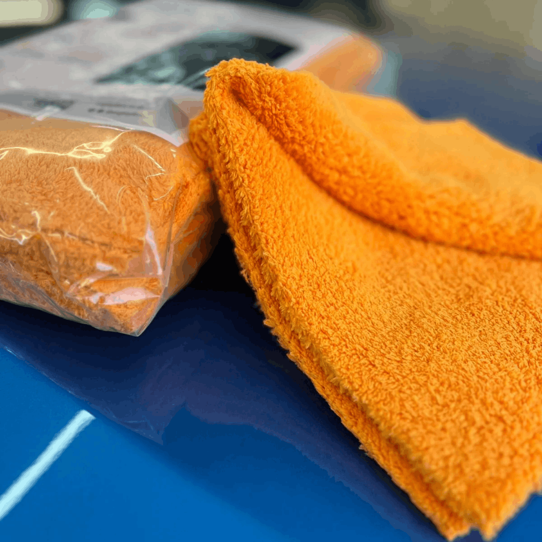 Orange plush microfibre detailing towel for car cleaning, buffing and polishing, shown on a vehicle paintwork.