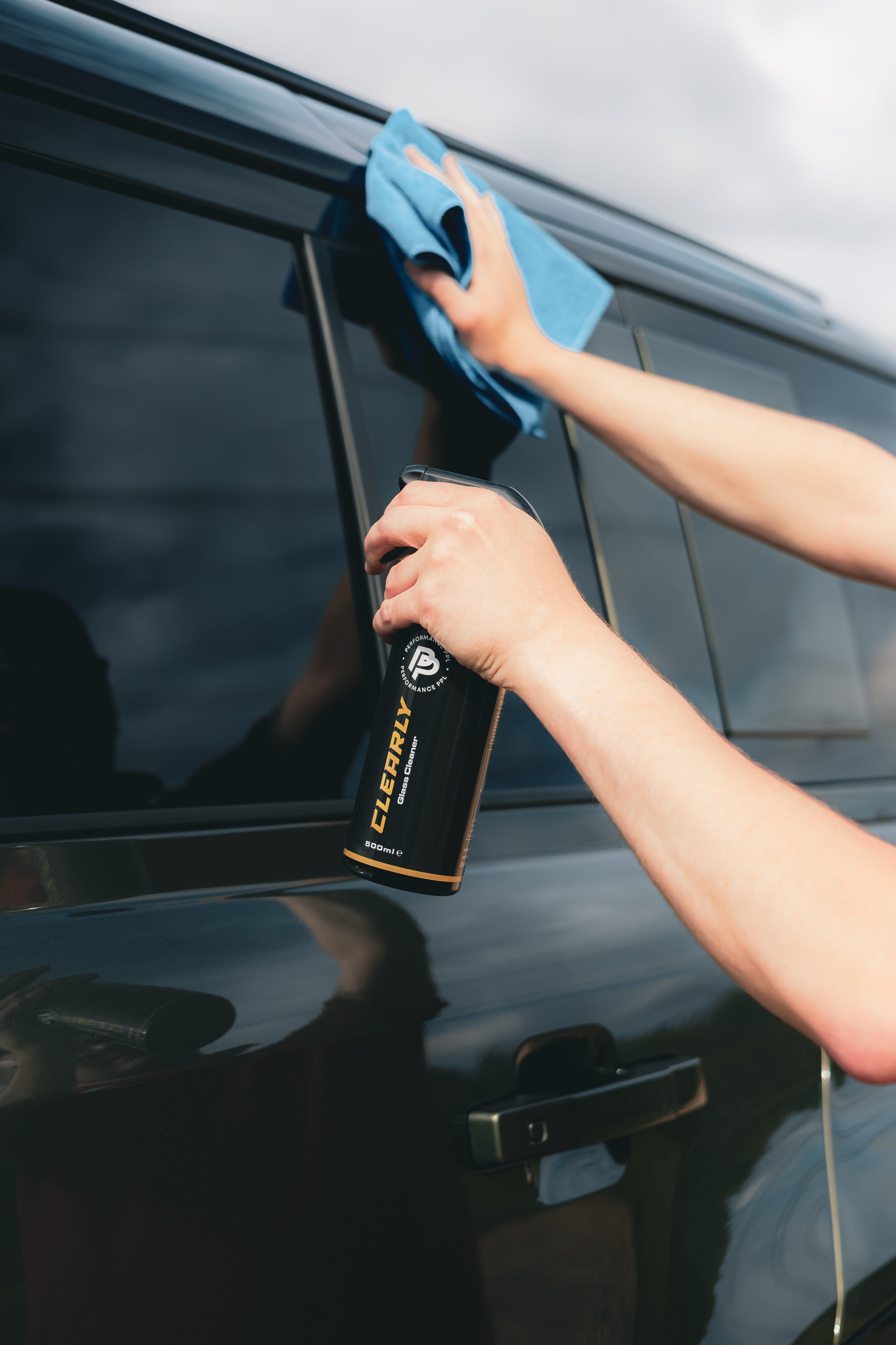 Person cleaning a car window with Performance PPL Clearly Glass Cleaner and a blue microfibre cloth.