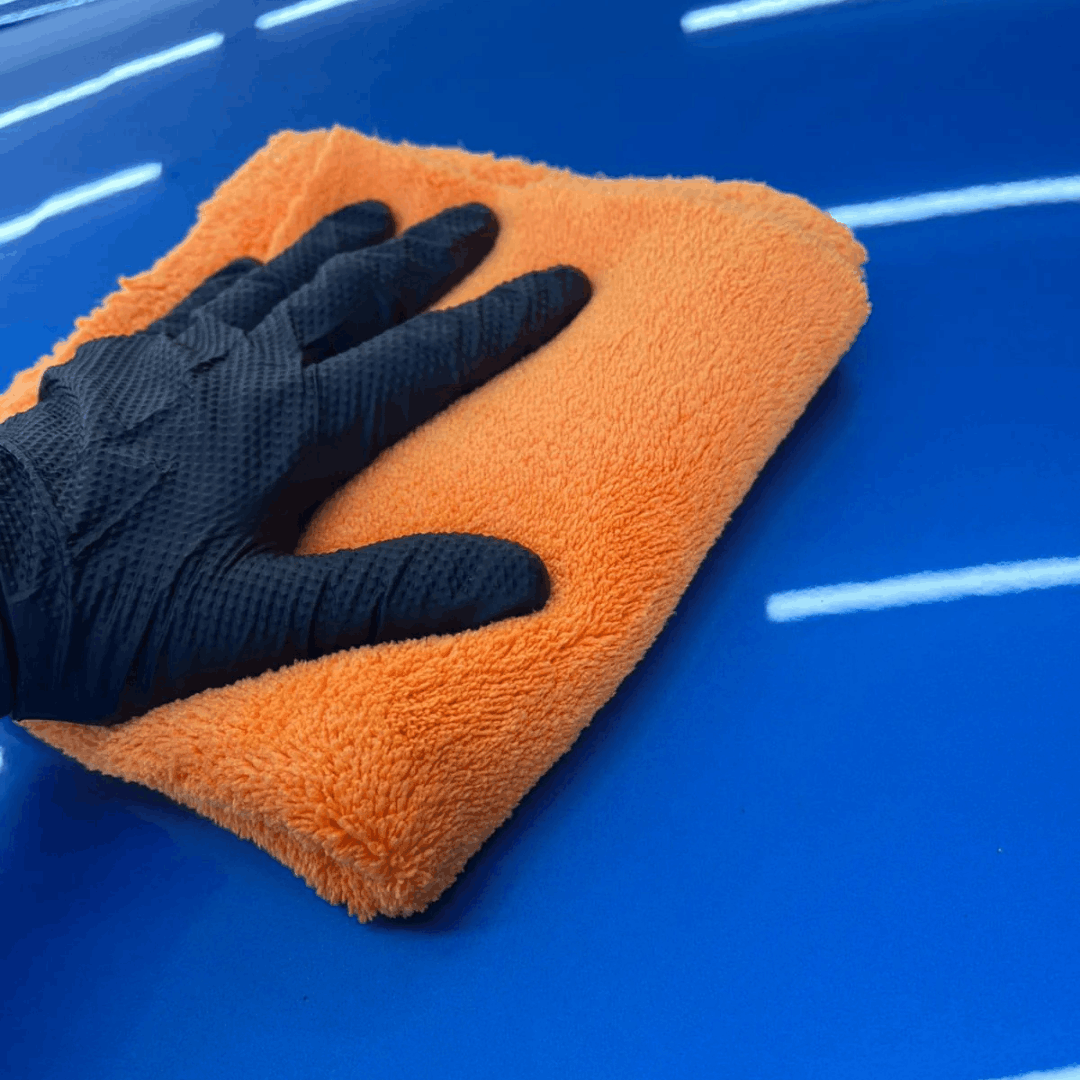 Orange plush microfibre detailing towel being used to buff and polish a car paintwork to a high-gloss finish.