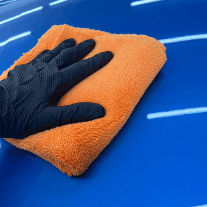 Orange plush microfibre detailing towel being used to buff and polish a car paintwork to a high-gloss finish.