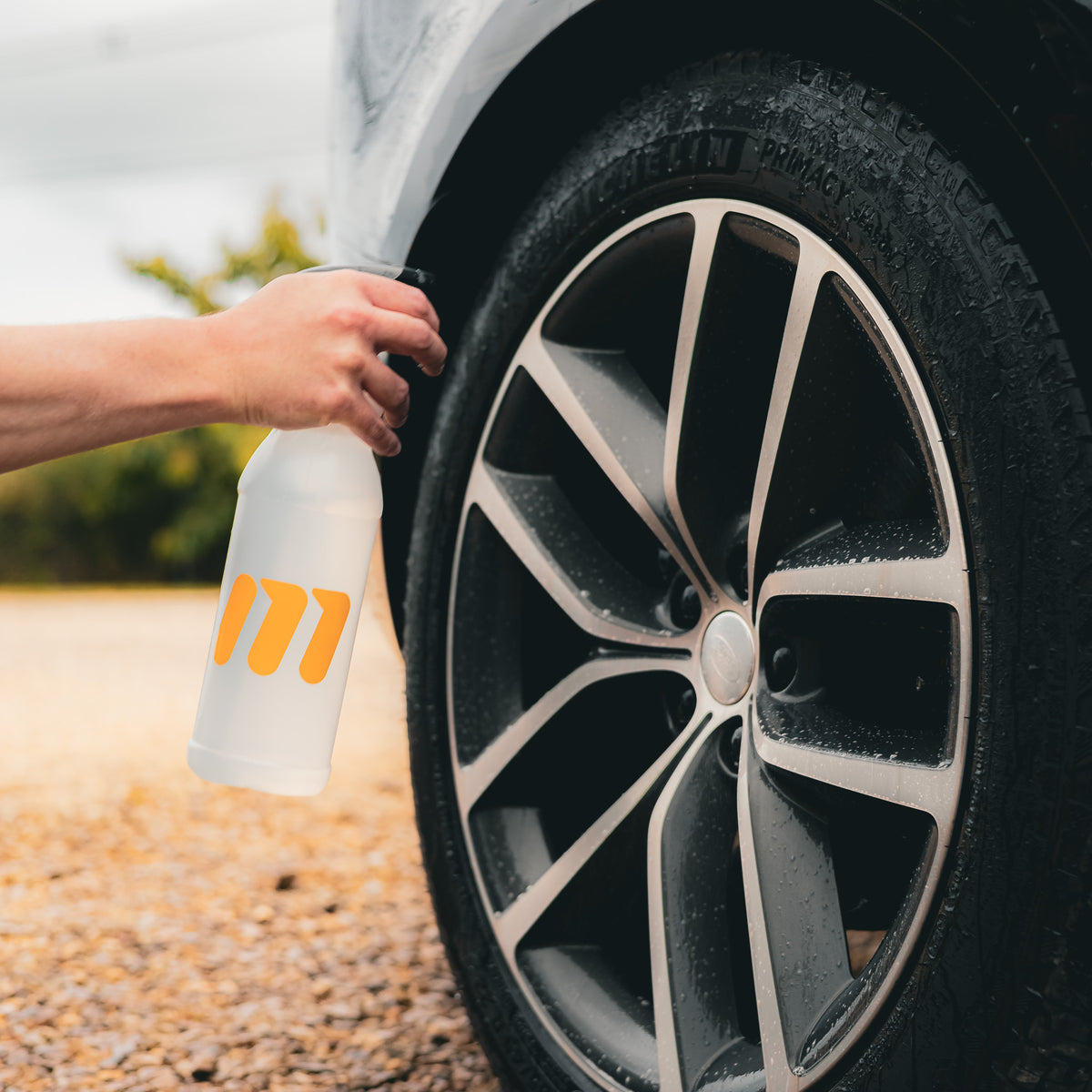 Car detailer spraying wheel cleaner onto an alloy wheel and tyre during a professional car wash.